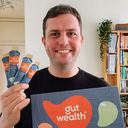 Person holding Gut Wealth products and smiling.