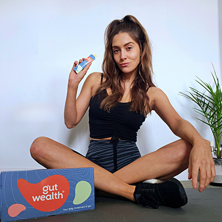 Person sitting cross-legged holding a small bottle, next to a box labeled 'gut wealth.'