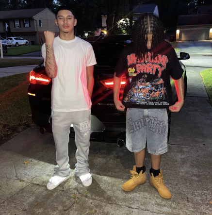 Two people stand in front of a black car at night.
