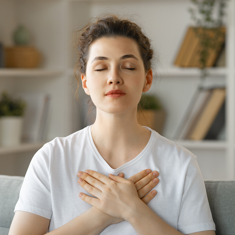 A woman sits on a couch with her eyes closed and hands crossed over her chest.