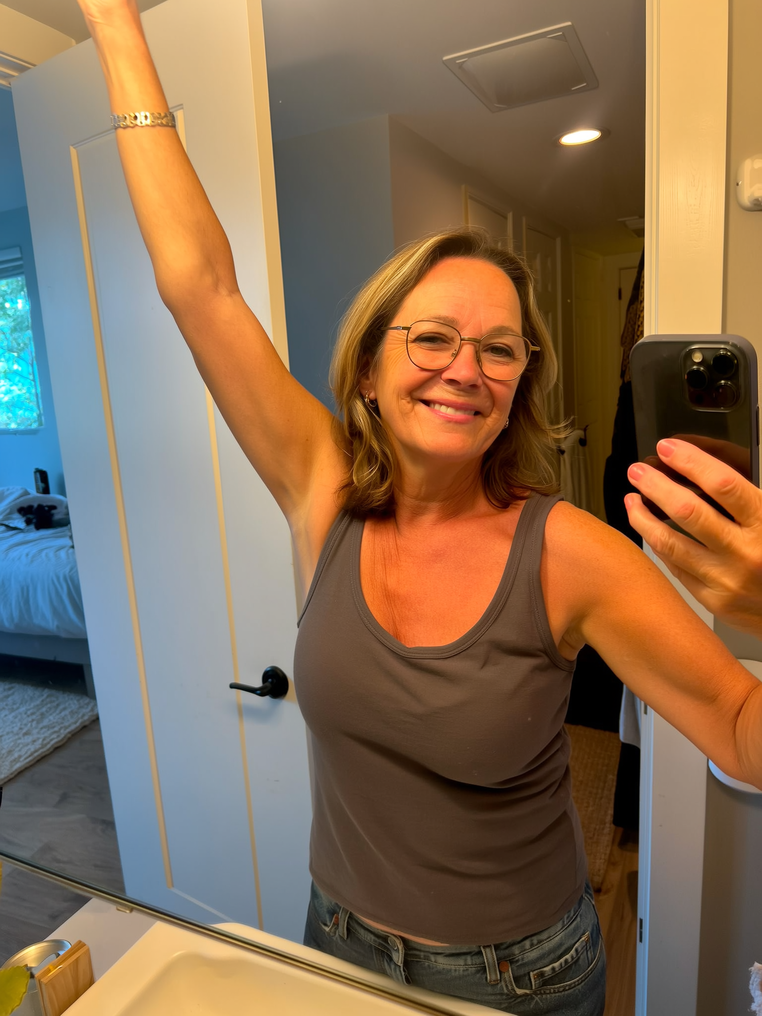 Person smiling in a mirror selfie with one arm raised.