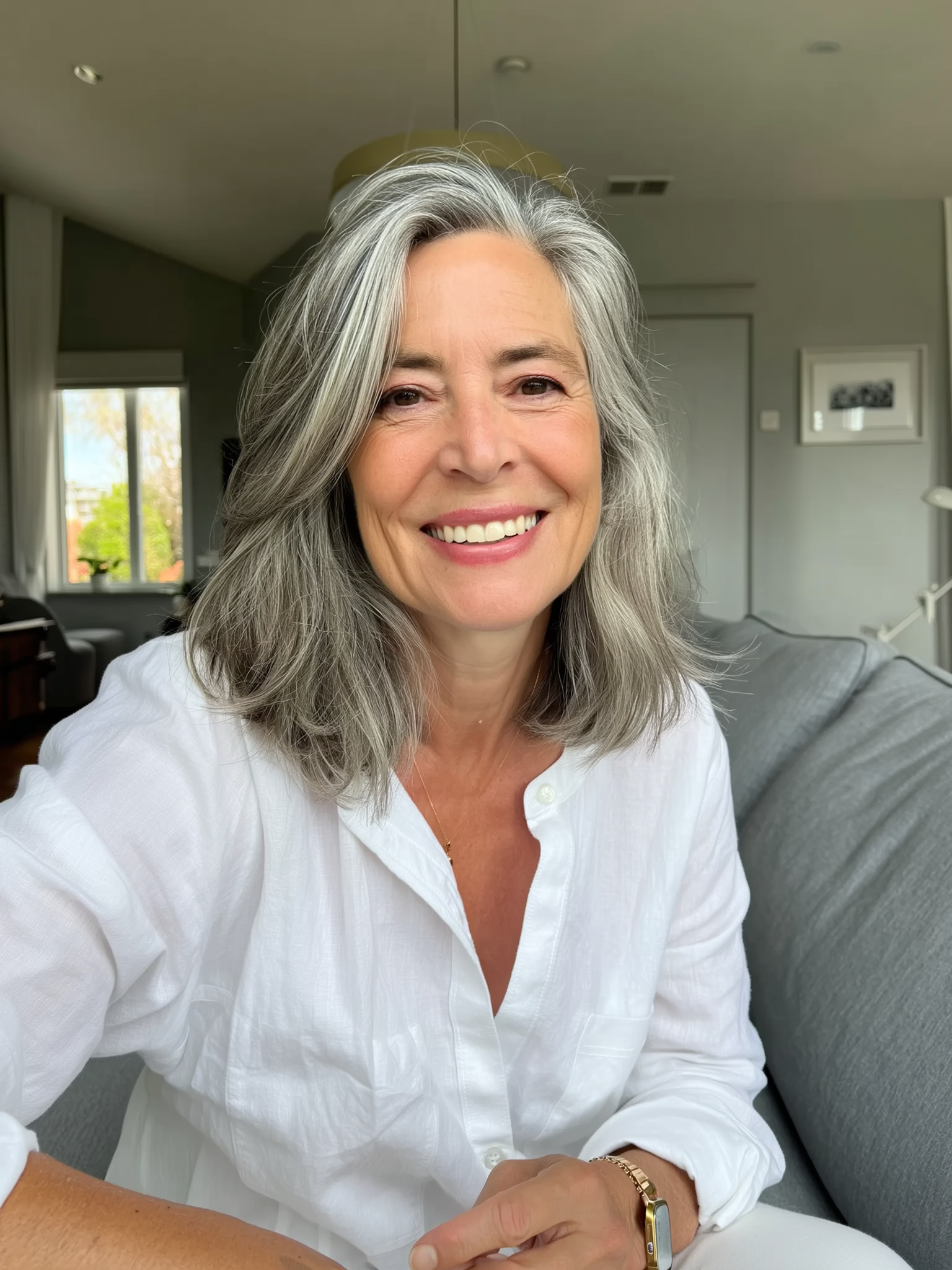 Person with gray hair smiling indoors, wearing a white shirt.