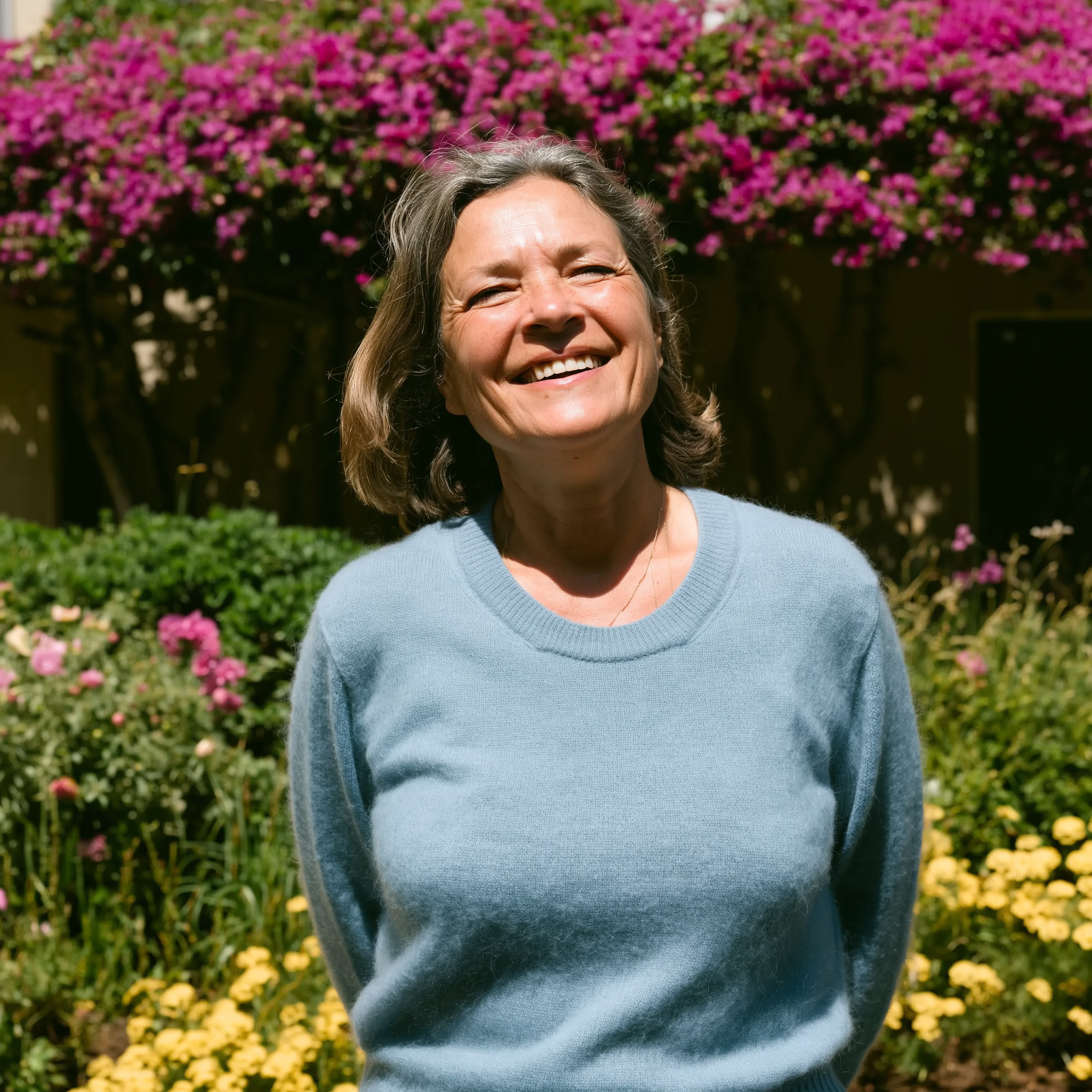Smiling person in blue sweater standing in front of vibrant flowers.
