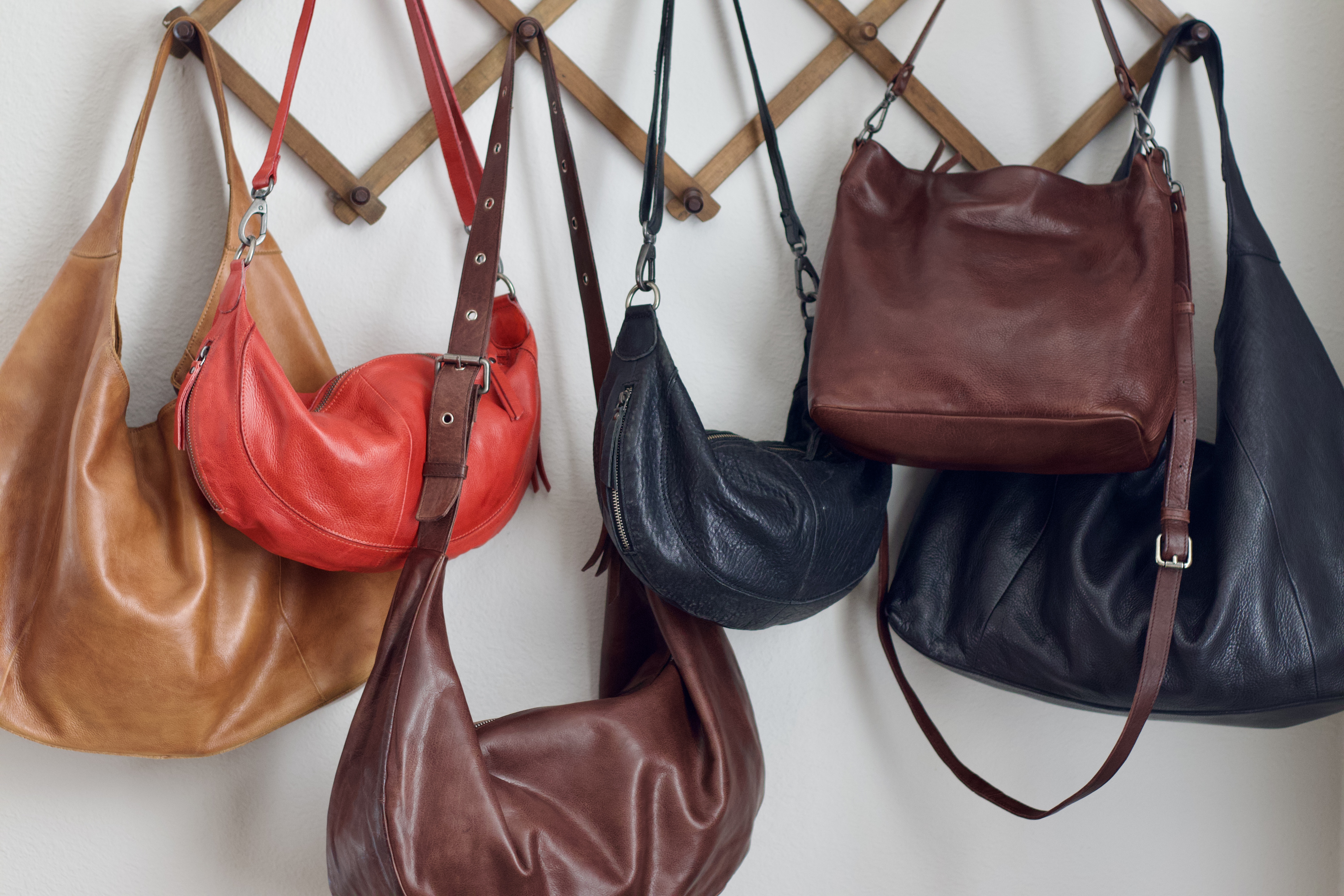 Several multi-colored leather purses hang on a wooden accordion rack against a white wall.