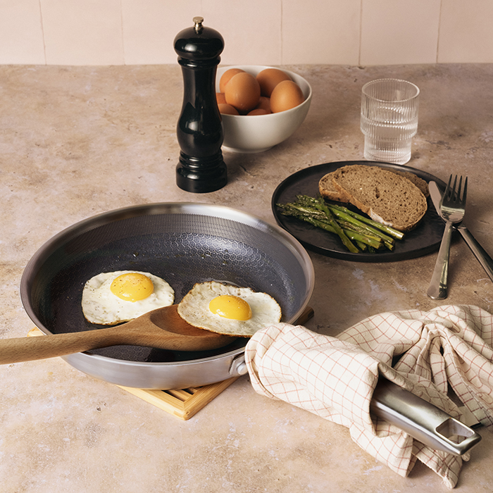 A frying pan with two fried eggs sits on a counter next to a plate of toast and asparagus.