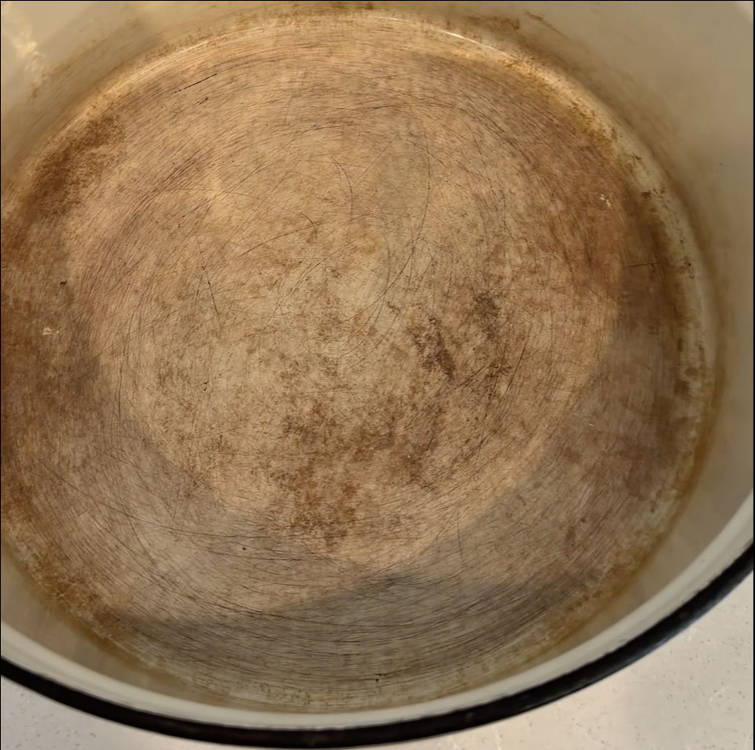 A top-down view of the inside of a heavily stained and scratched cooking pot.
