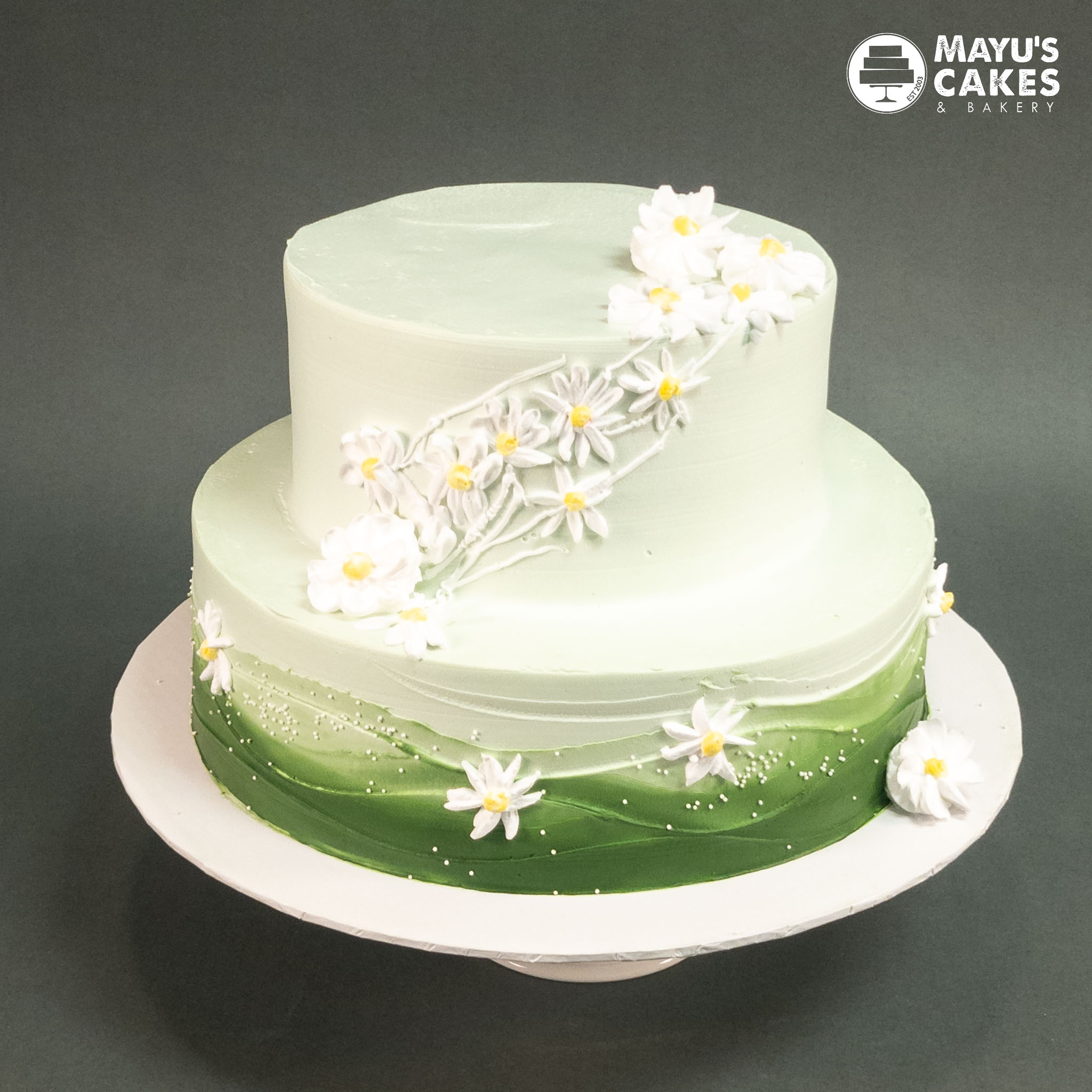 Two-tiered green cake with white floral decorations.