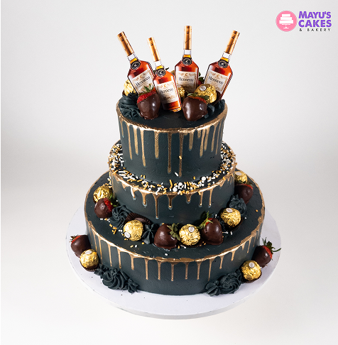 Three-tiered cake with chocolate bottles and gold decorations.