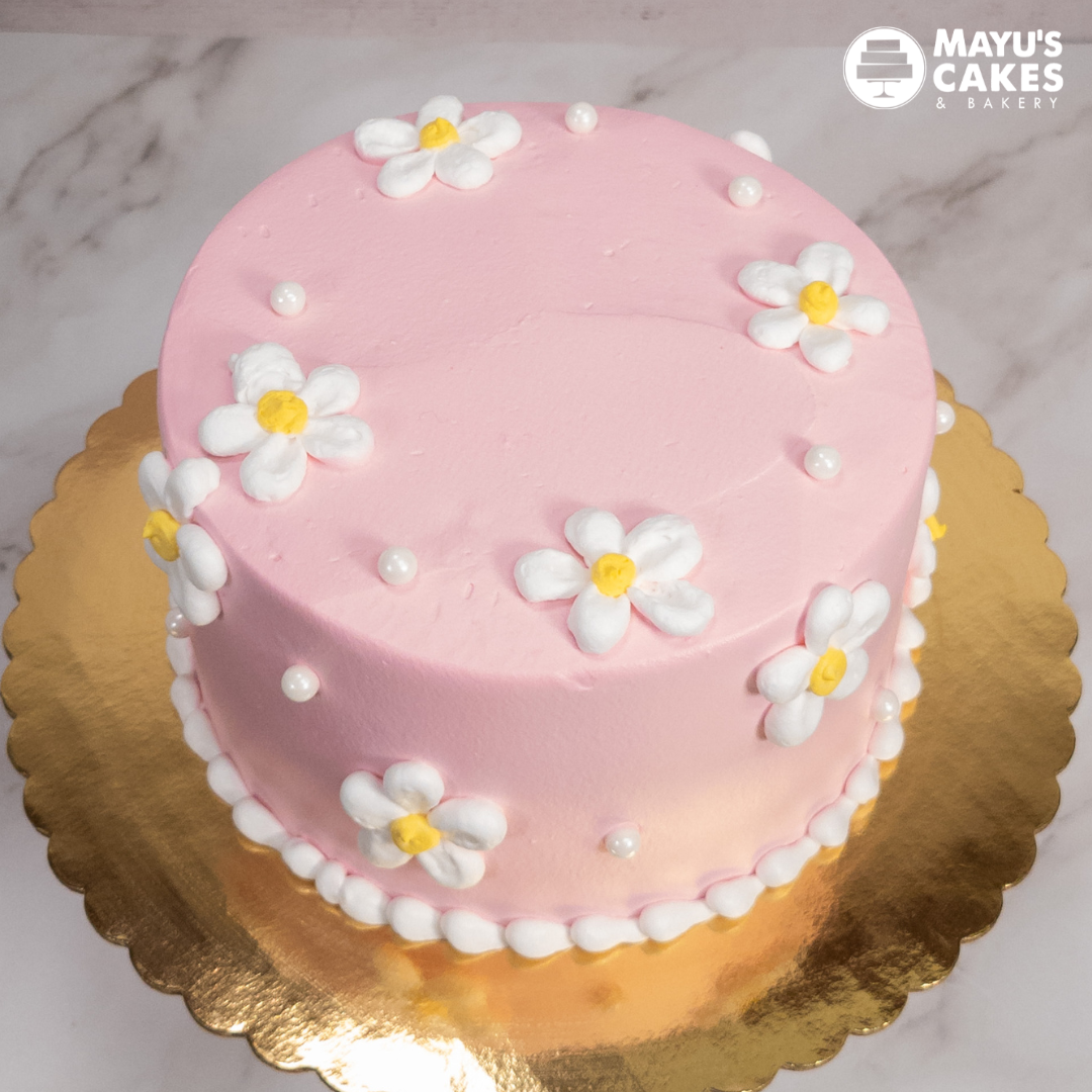 Pink cake with white flowers and pearls on a gold board.