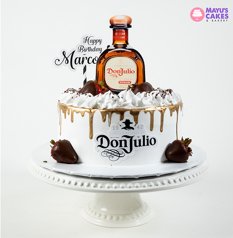 White cake with chocolate drips, strawberries, and a Don Julio bottle on top.
