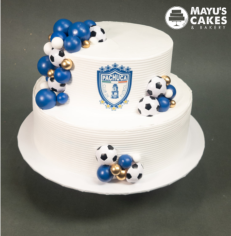 Two-tier cake with Pachuca logo, soccer balls, and blue and gold decorations.