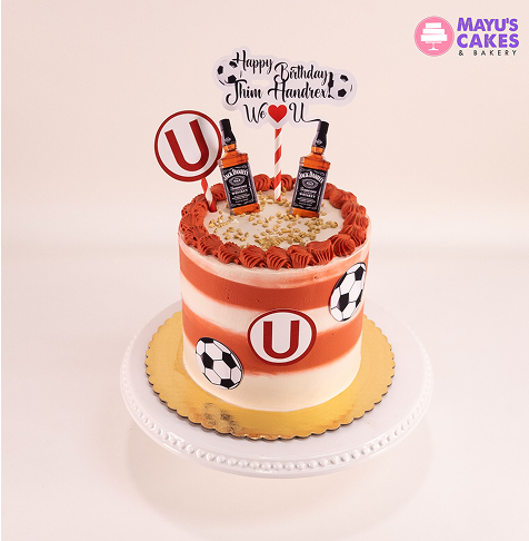 Striped cake with soccer and whiskey decorations, birthday message on top.