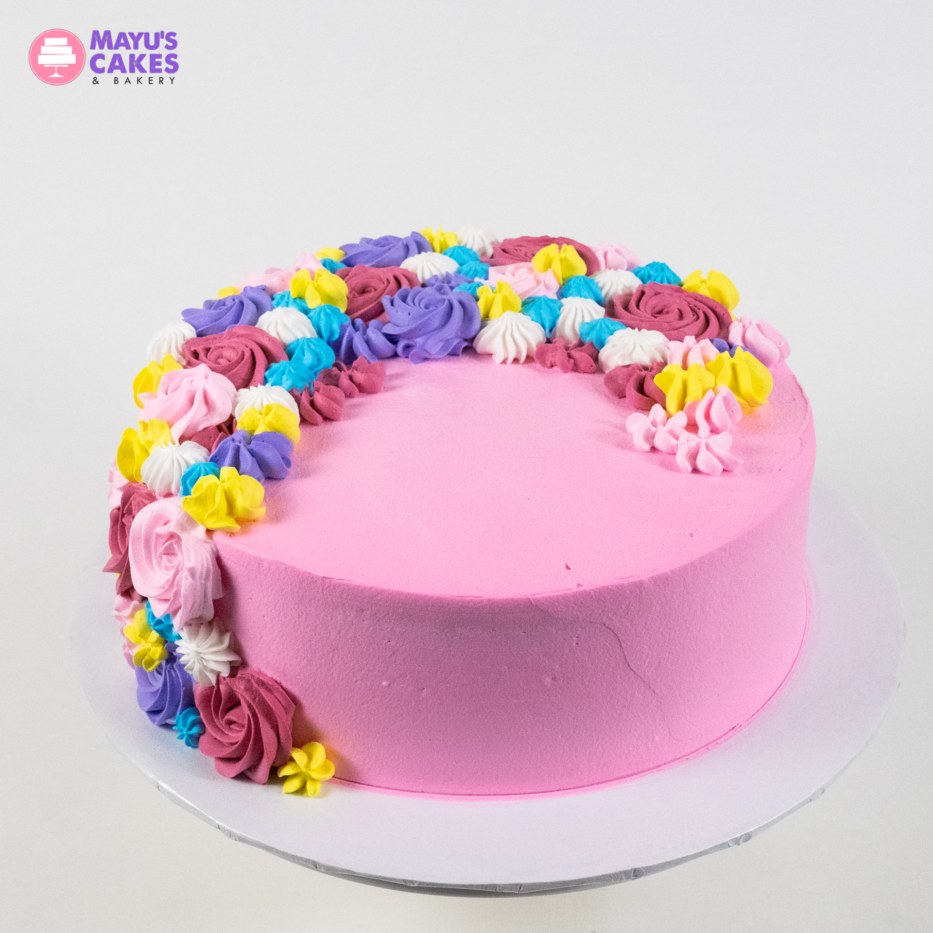 Pink cake with colorful floral icing decorations on top.