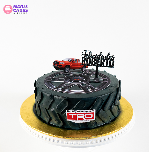A cake designed like a tire with a toy truck and 'Felicidades Roberto' topper.