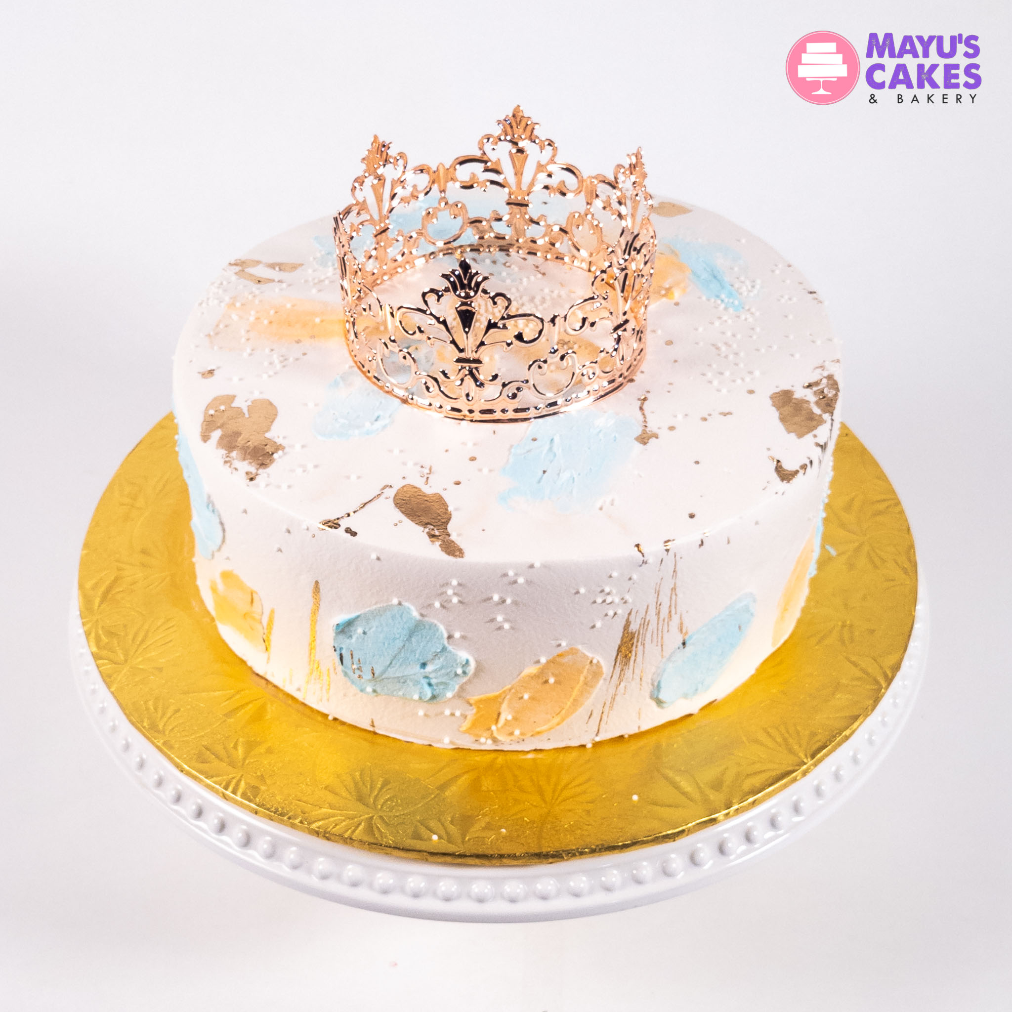 Decorated cake with a gold crown on top, colorful brushstrokes, on a white and gold stand.