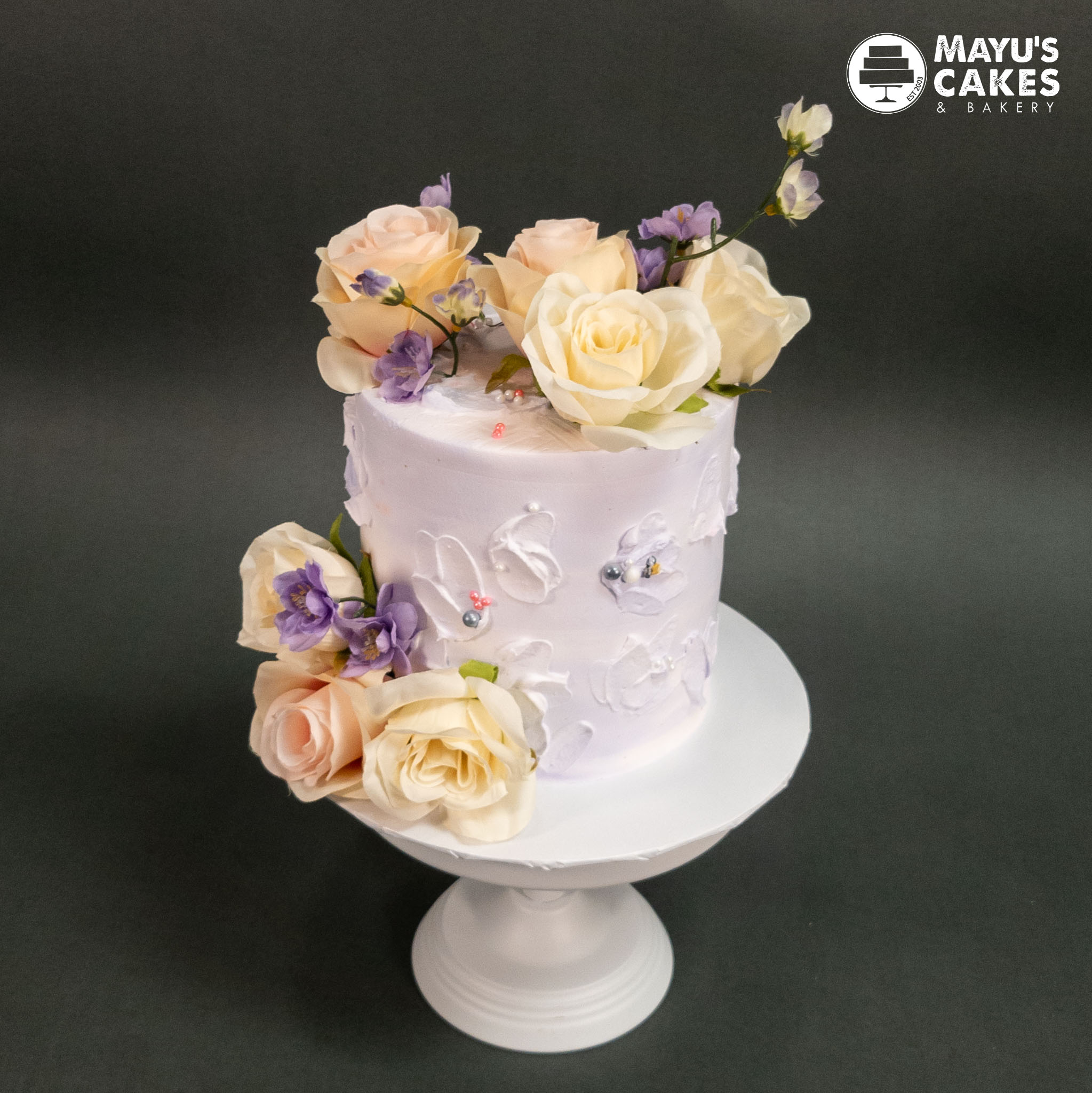 White cake with pastel flowers on a white stand.