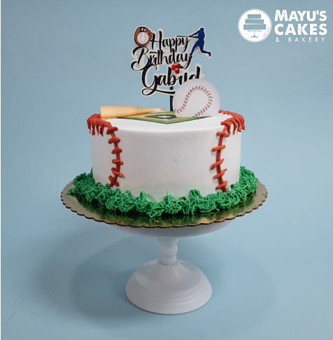 Baseball-themed birthday cake with green icing and a topper on a white stand.