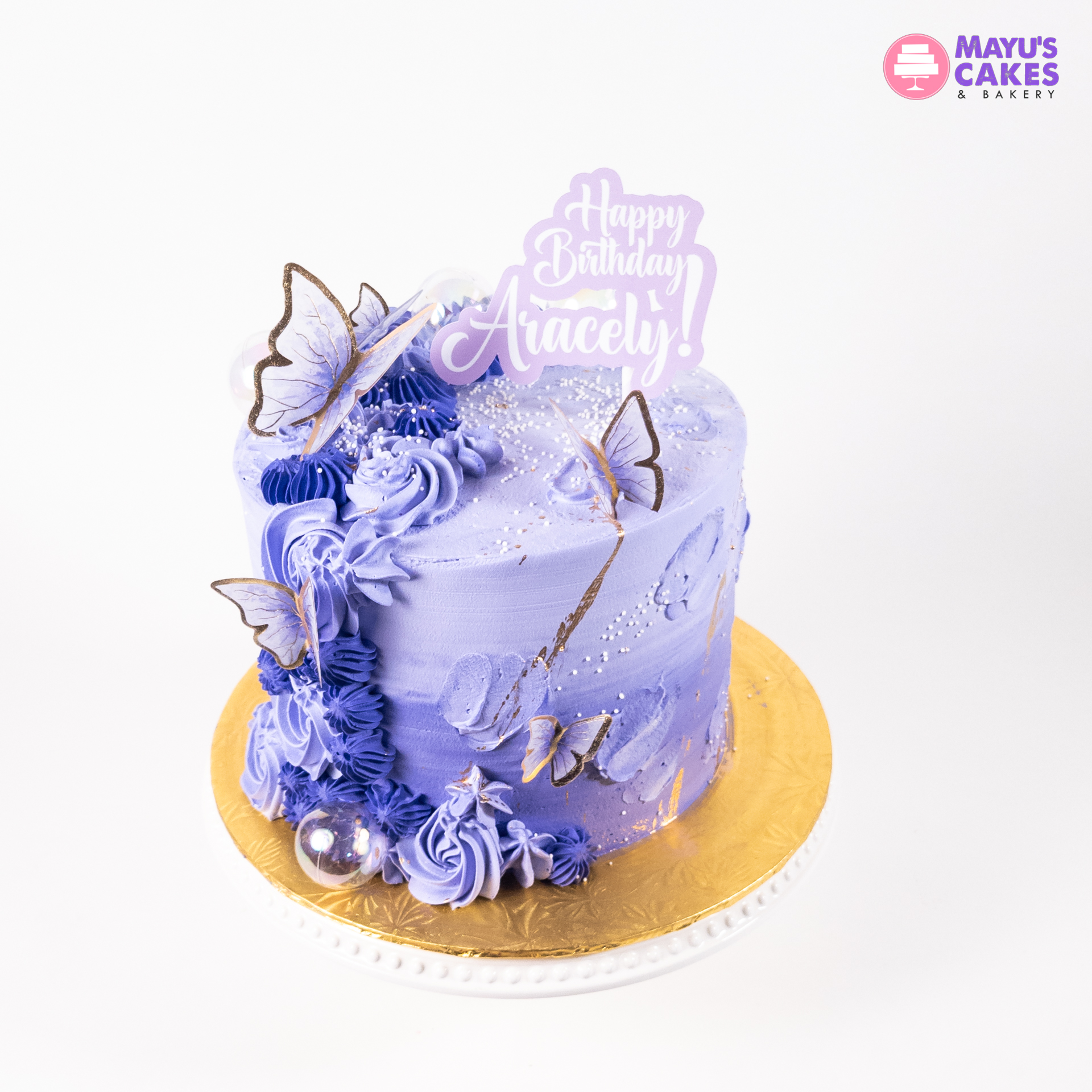 Purple birthday cake with butterfly decorations and 'Happy Birthday Aracely' topper.