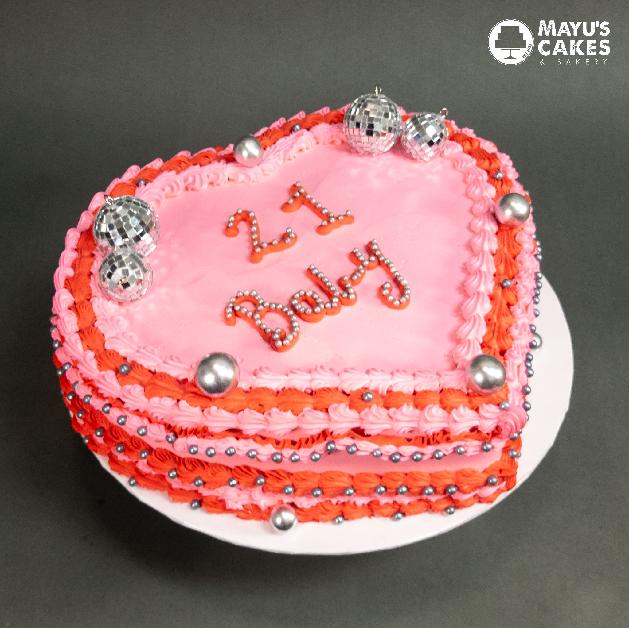 Heart-shaped pink cake with '21 Baby' and silver decorations.