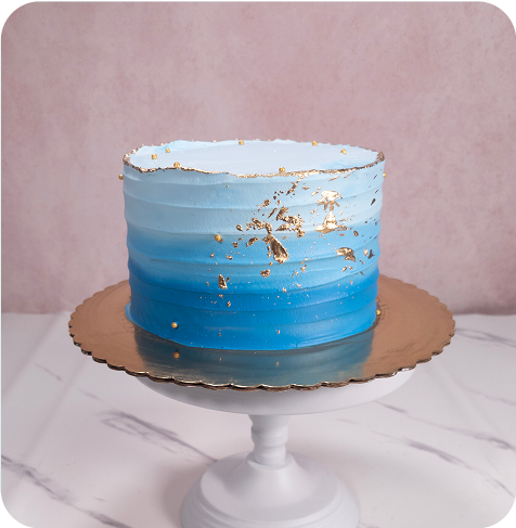 Blue ombre cake with gold accents on a white cake stand.