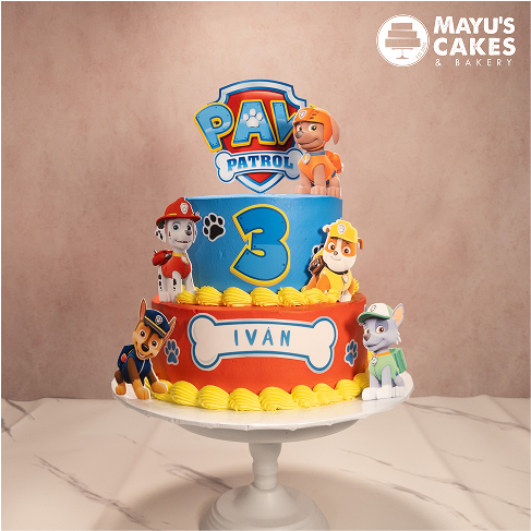 Colorful Paw Patrol-themed cake with character figurines and the name 'Ivan' on a bone-shaped plaque.