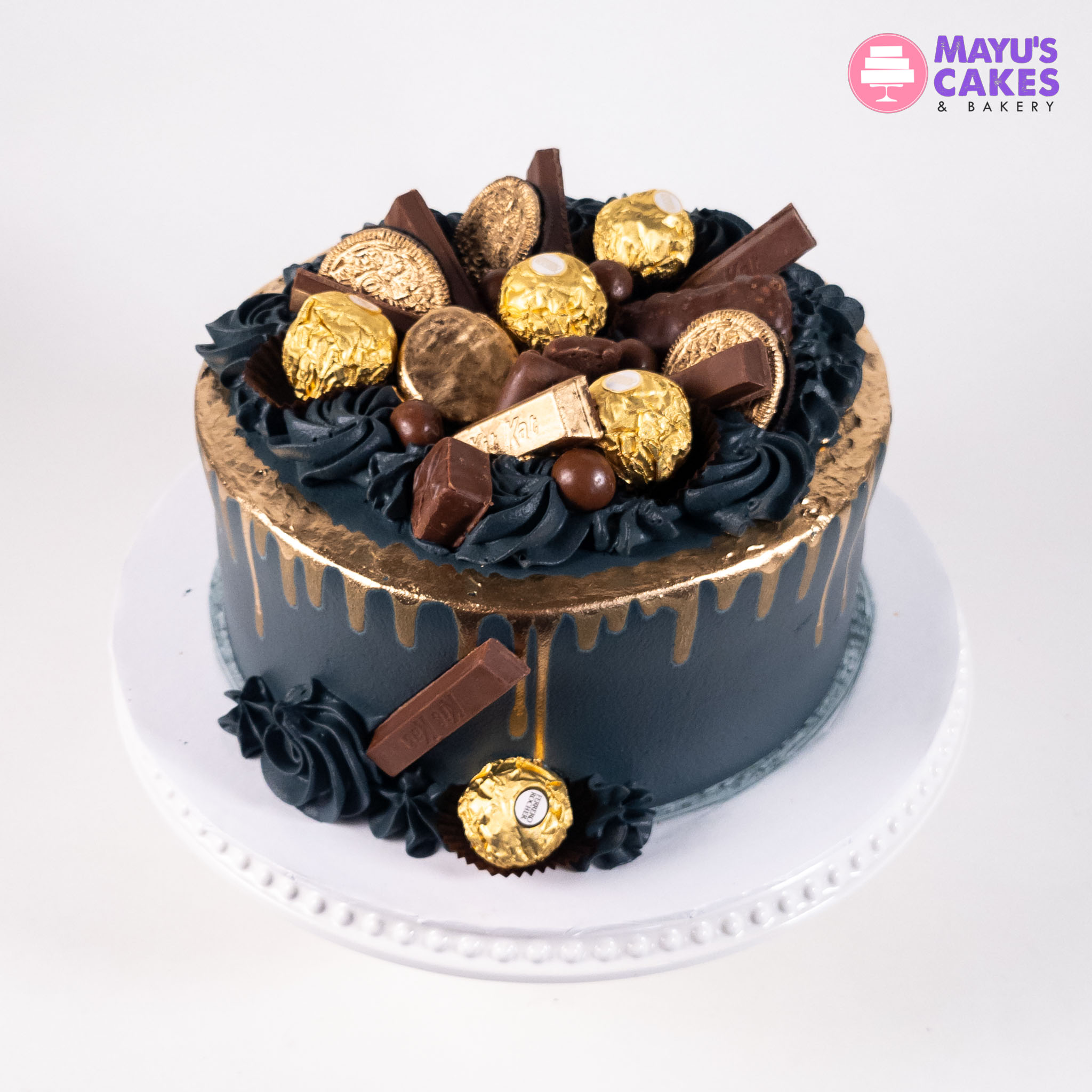 Black and gold cake topped with assorted chocolates and gold-wrapped candies.