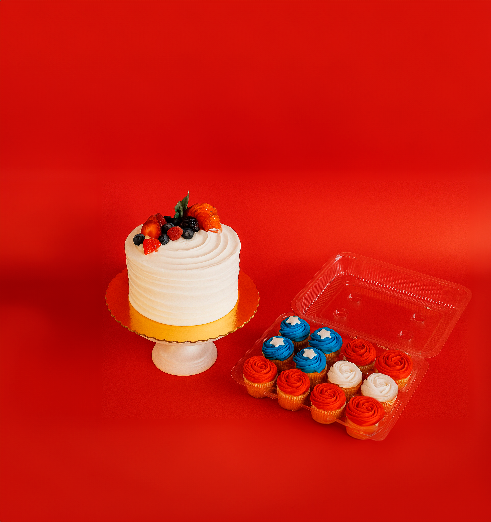 White cake with fruit and colorful cupcakes on a red background.