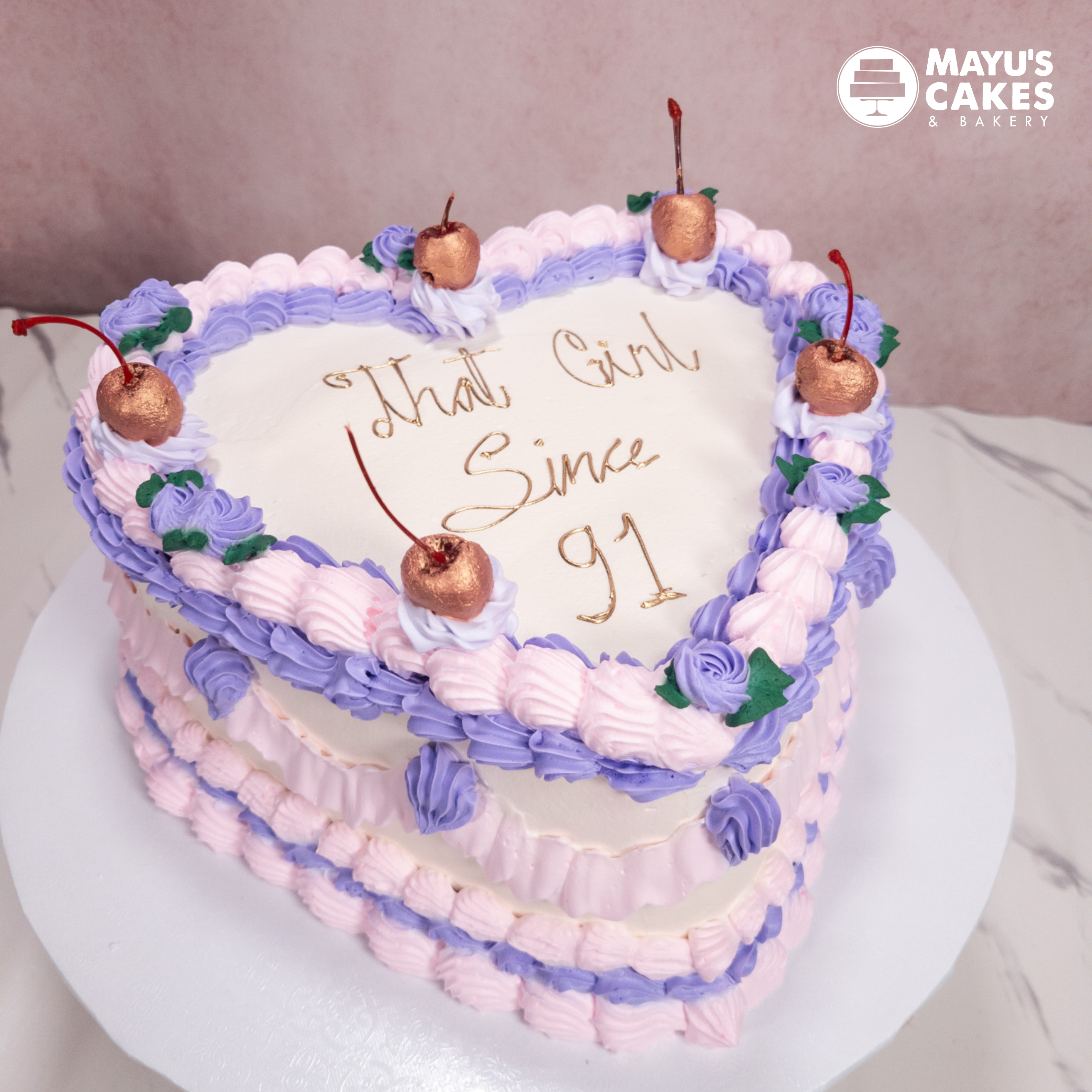 Heart-shaped cake with purple and pink frosting, cherries, and 'That Girl Since 91' written on top.