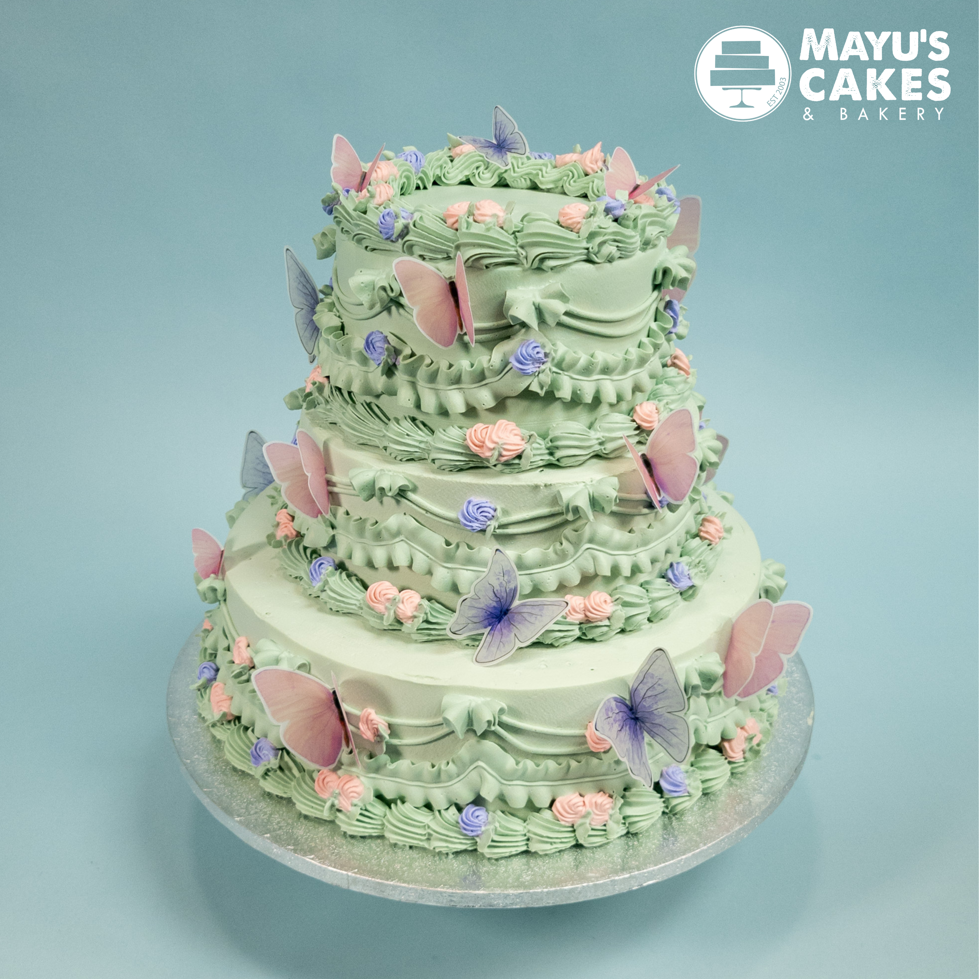 Three-tiered green cake with pink and purple butterfly decorations.