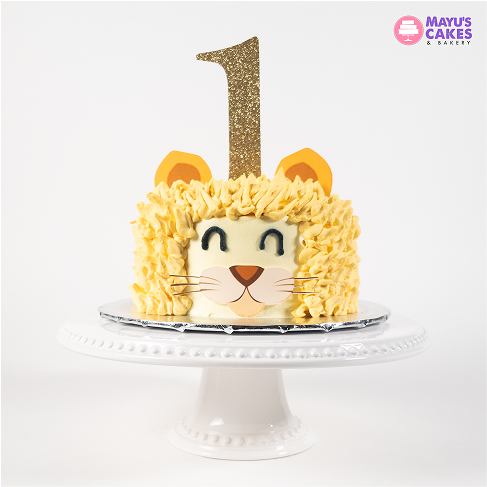 Lion-themed cake with a glittery number one topper on a white stand.