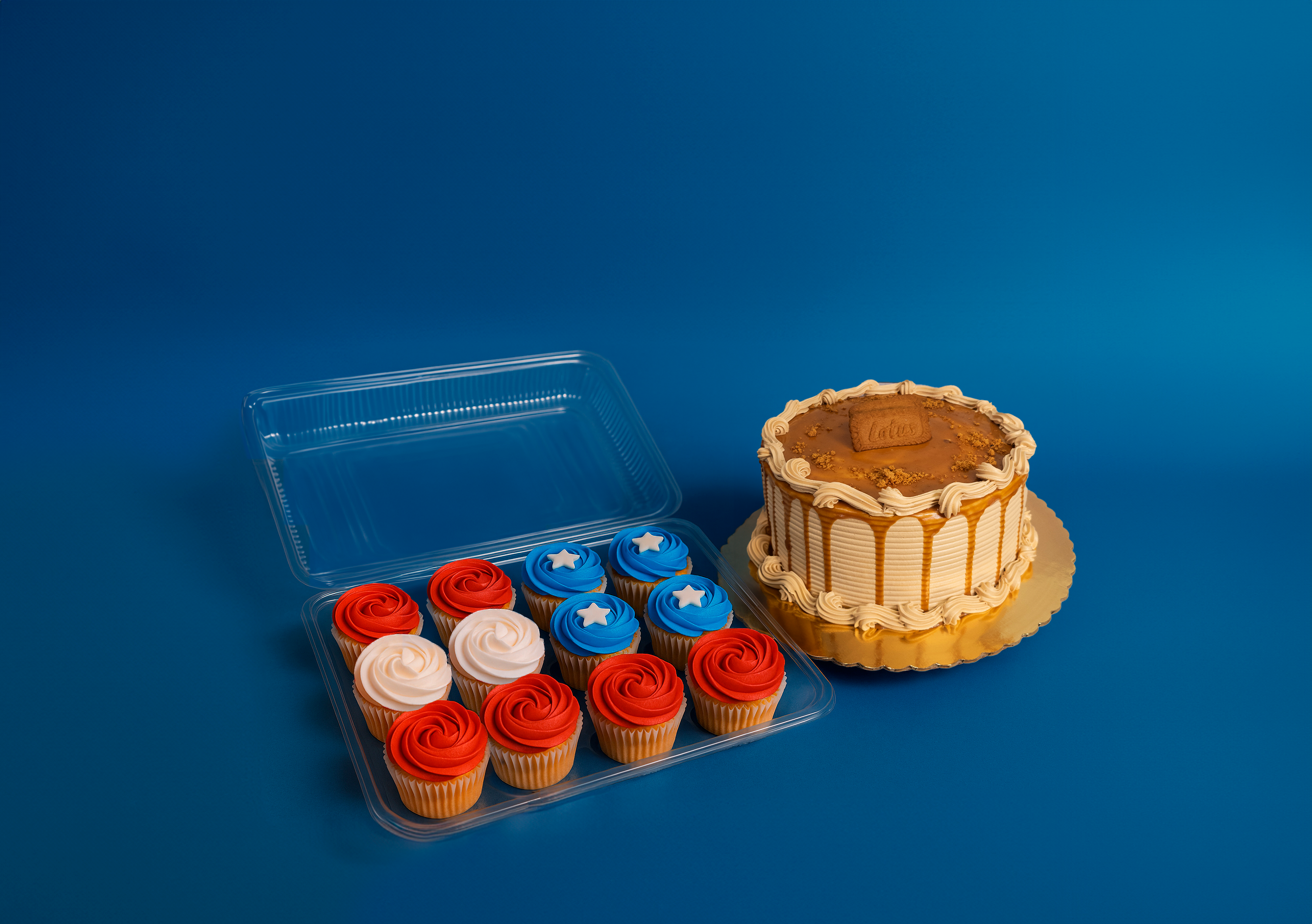 Cupcakes in a plastic container and a decorated cake on a blue background.