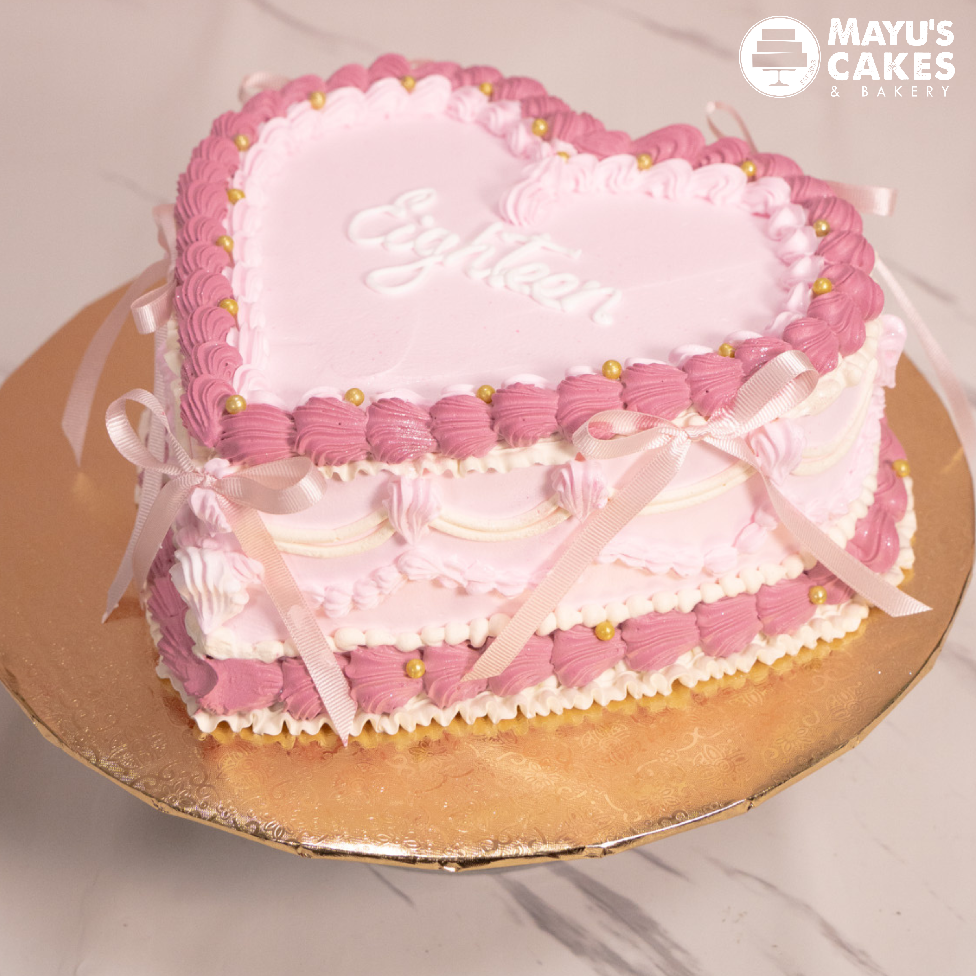 Heart-shaped pink and white cake with 'Eighteen' written on top.