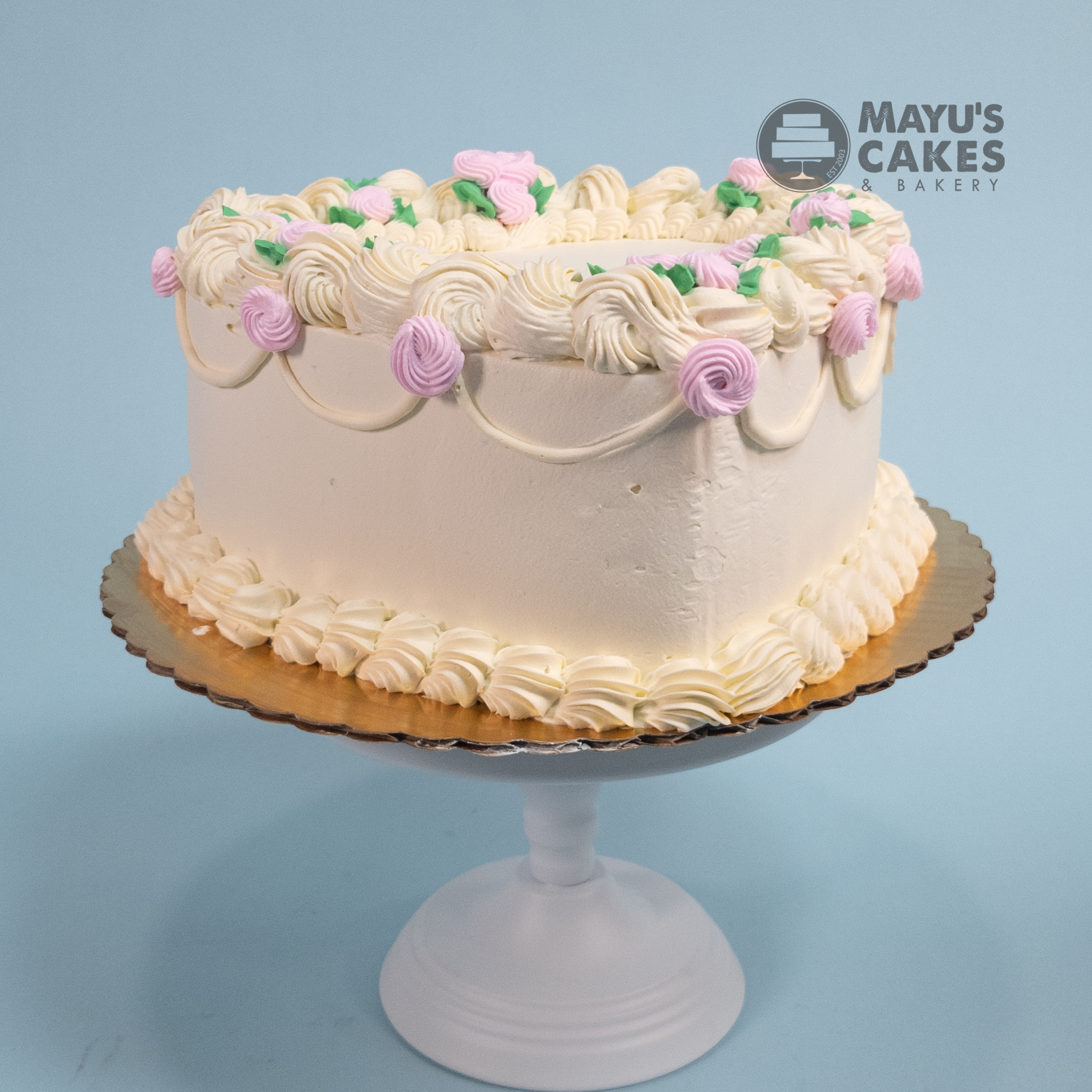 White frosted cake with pink and green decorations on a cake stand.