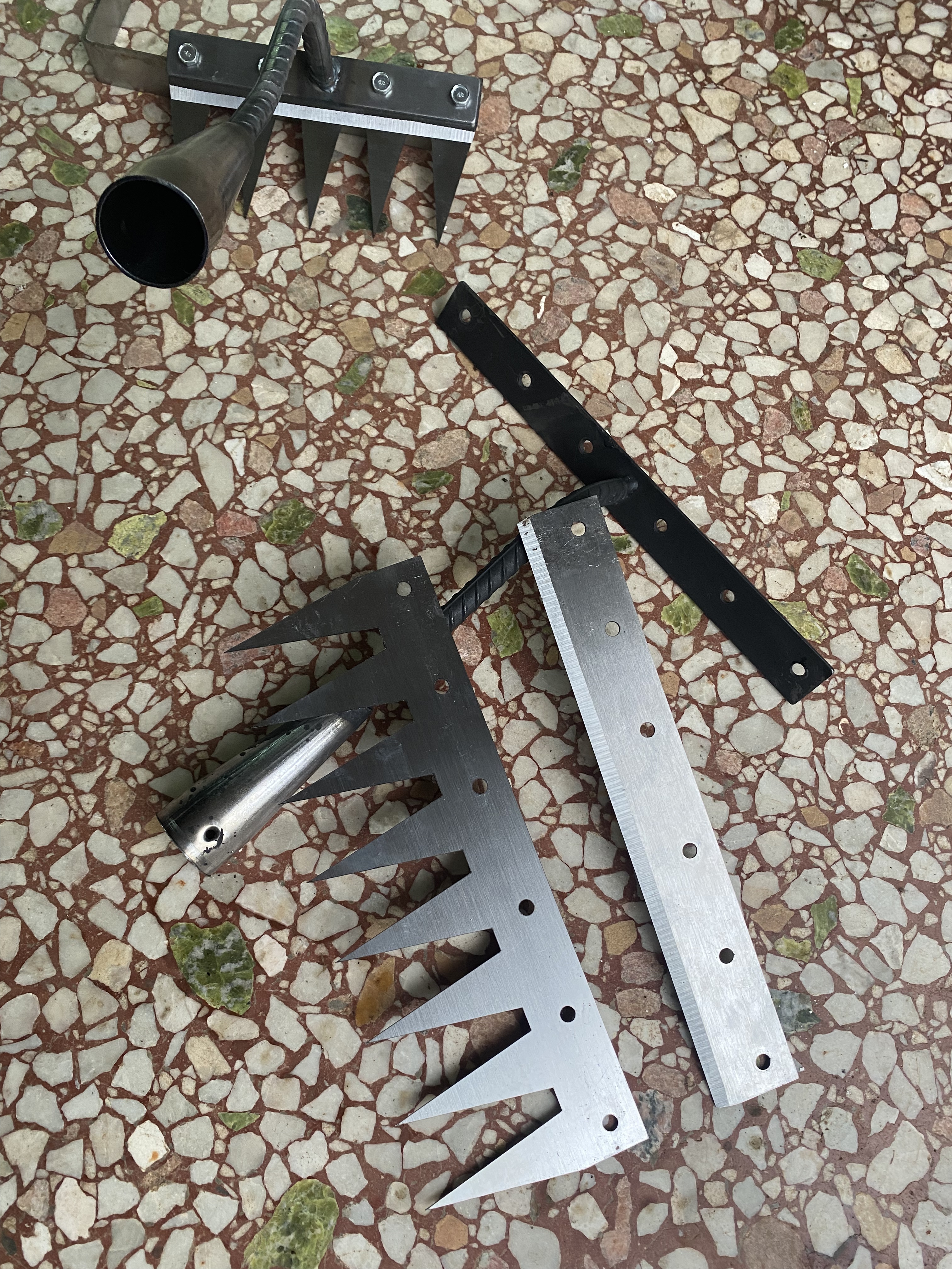 A metal hand tool with three sharp prongs and a textured handle on a light surface.
