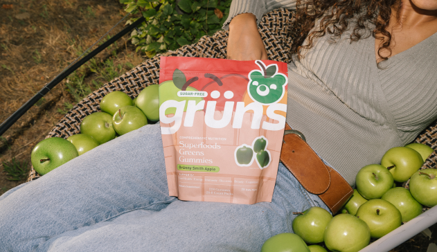 Person with green apples and a package of 'grüns Superfoods Greens Gummies.'