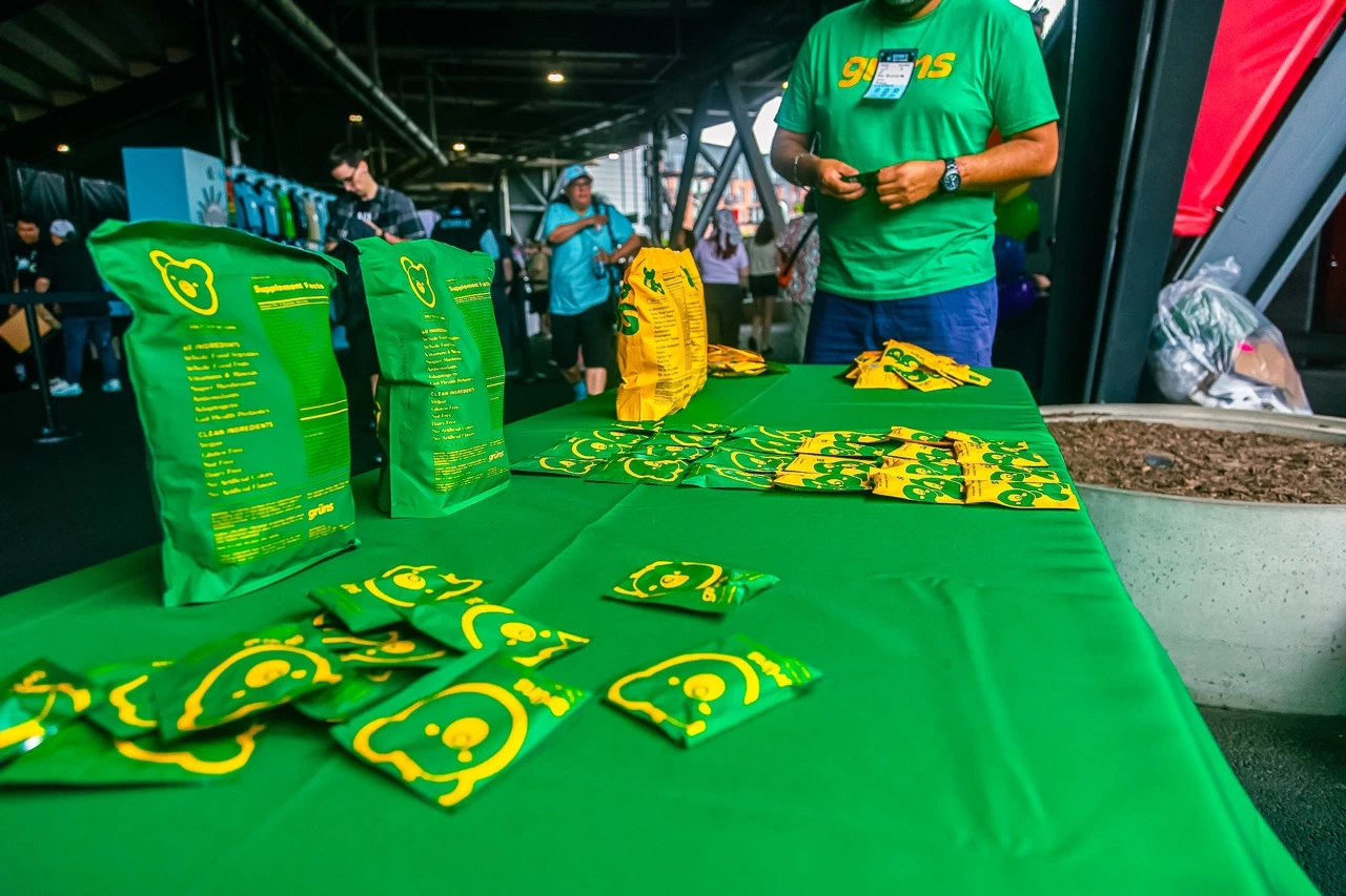Green table with packaged snacks and a person standing behind it.