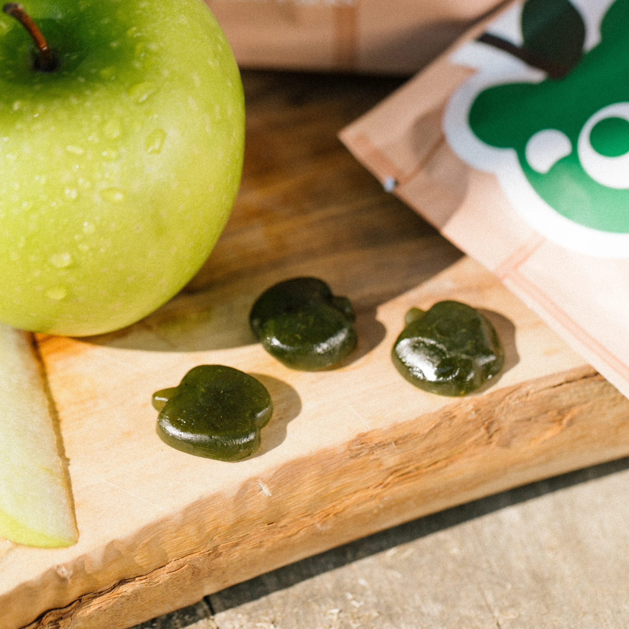 Green apple and apple-shaped gummies on a wooden board.