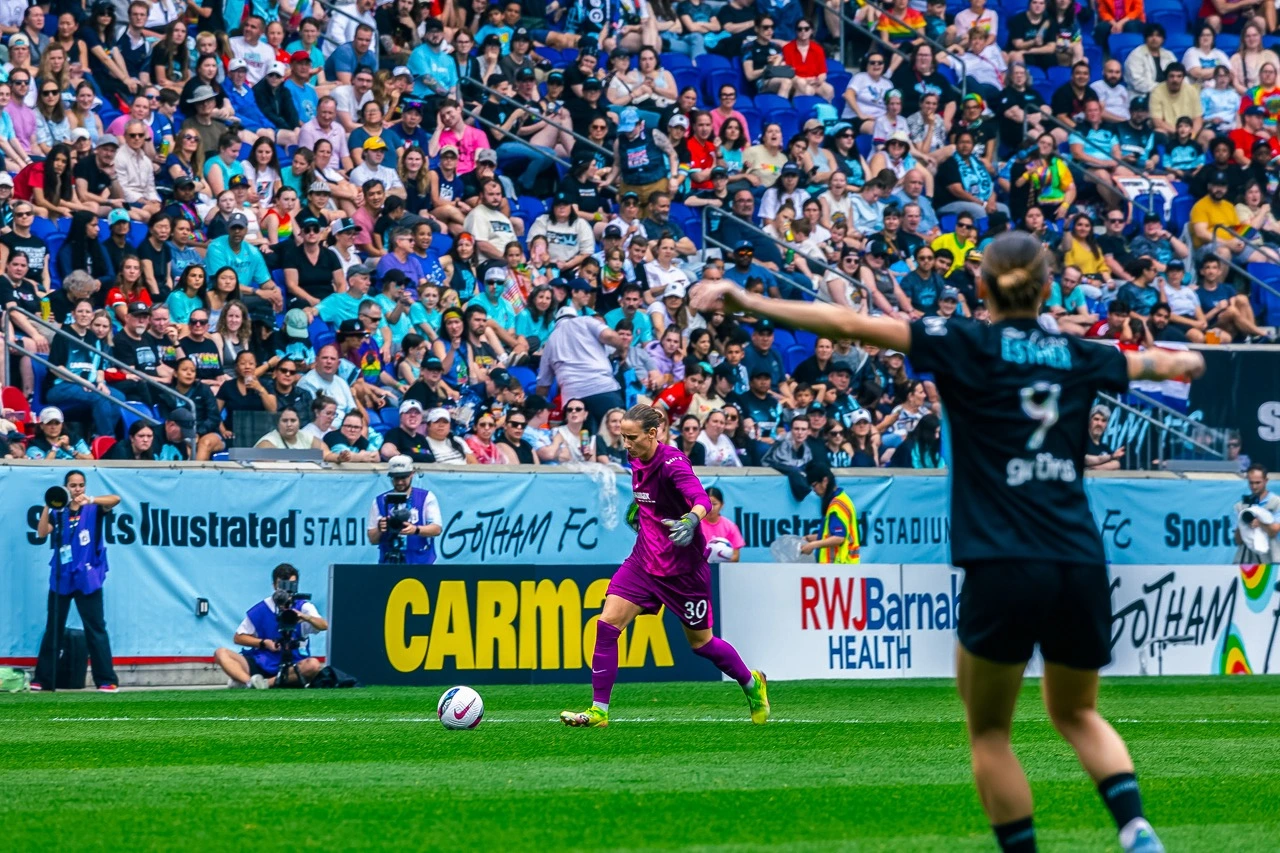 Soccer match with a goalkeeper in pink and a player in black, crowded stadium background.