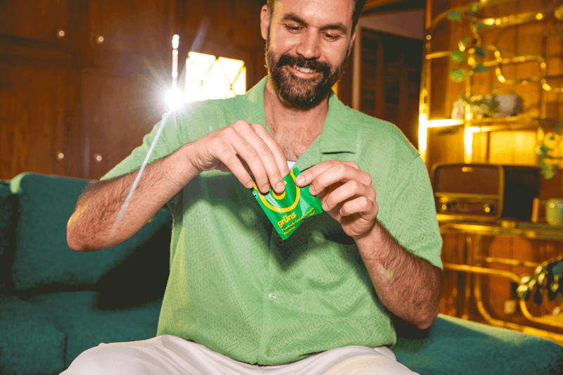 Man in green shirt opening a packet, sitting on a teal couch.