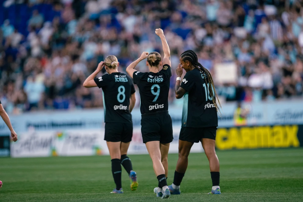 Three soccer players in black jerseys celebrating on the field.
