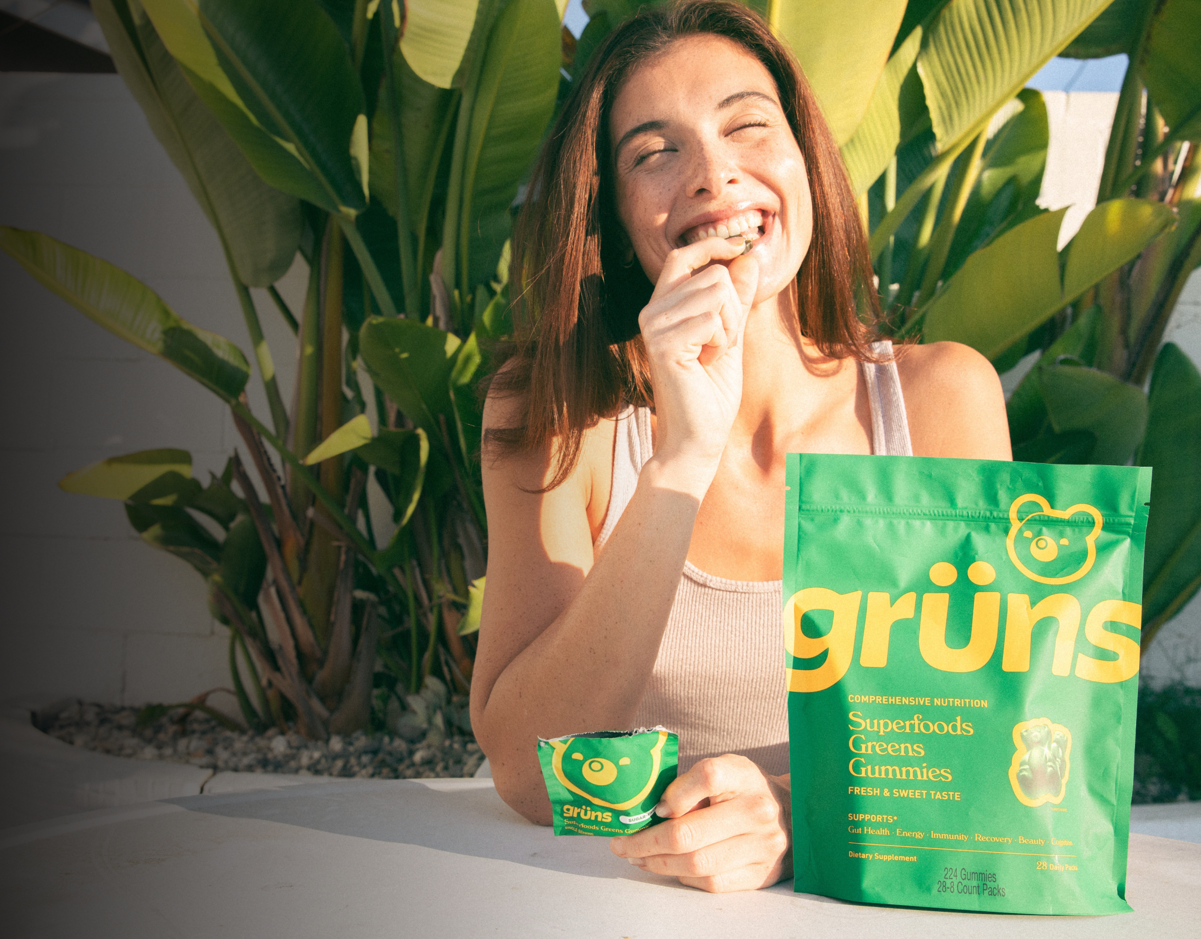 Person smiling and eating green gummies next to a bag labeled 'grüns'.