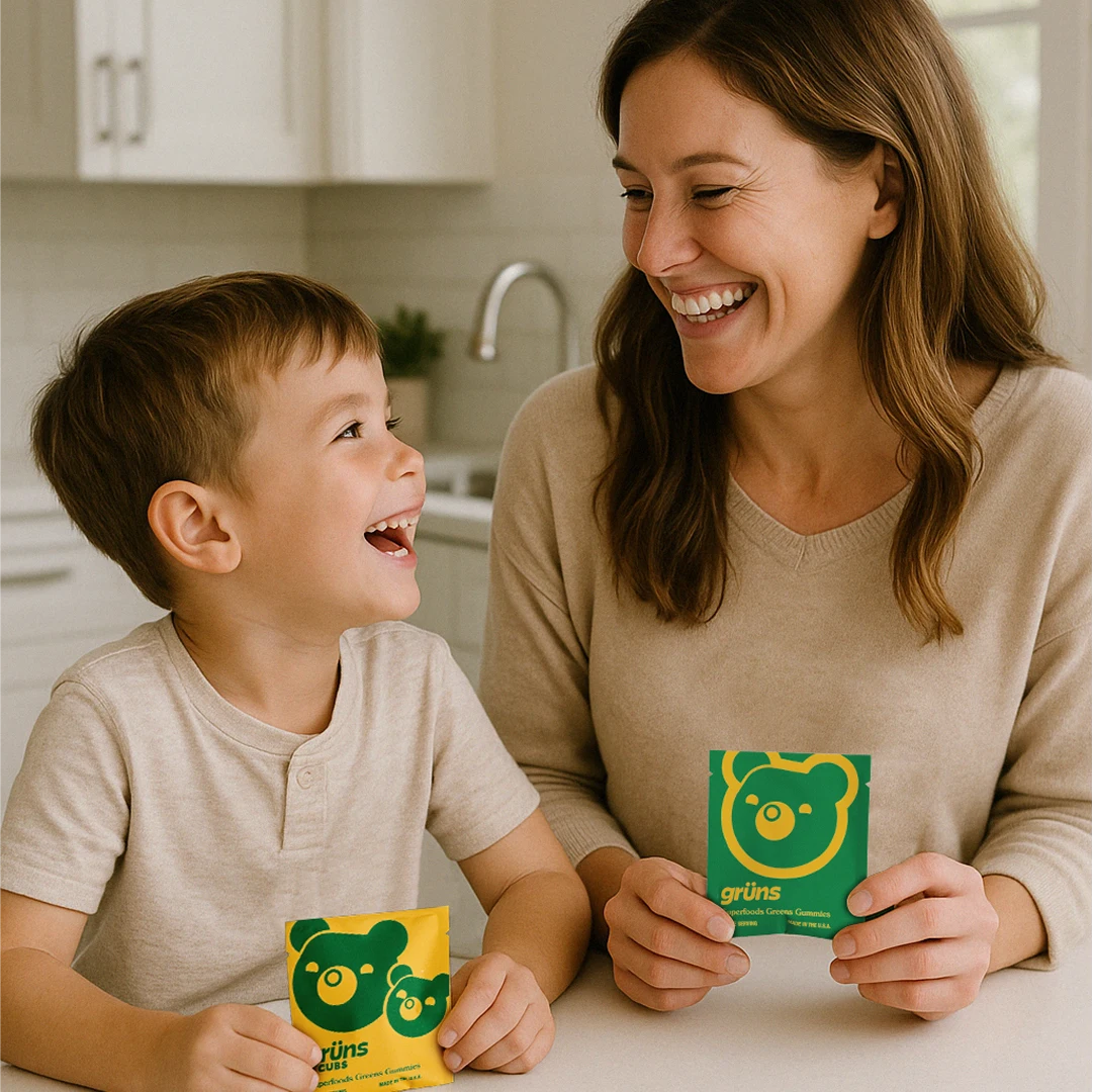 Smiling woman and child holding green and yellow packets in a kitchen.