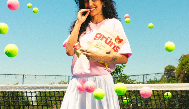 Person holding snack bag, surrounded by colorful tennis balls, standing in front of a net.