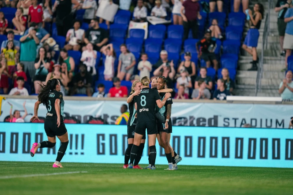 Soccer players celebrating a goal on the field with cheering crowd in background.