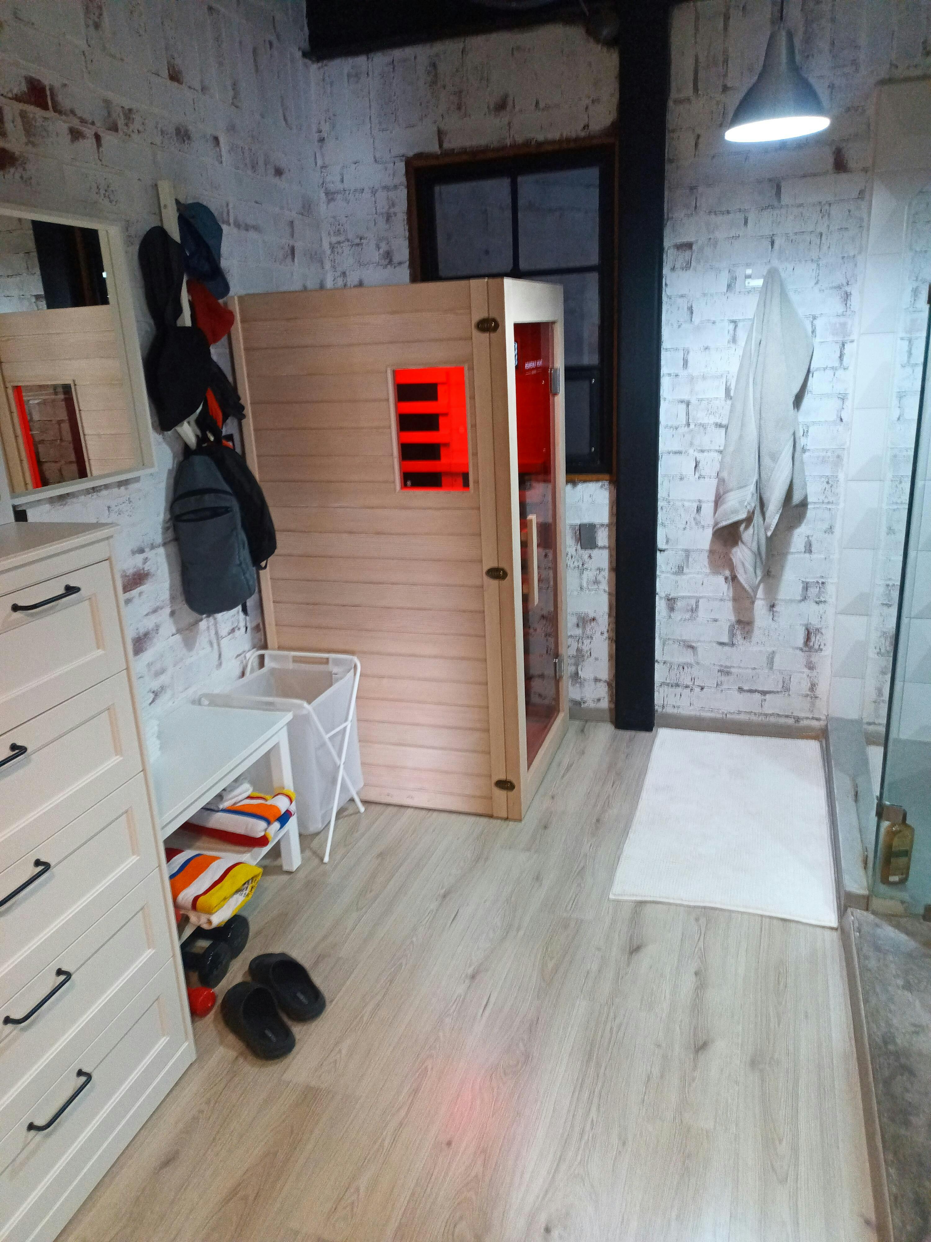Room with a small sauna, towels, slippers, and a hanging towel.