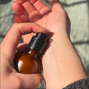 A person applying a product from a brown glass pump bottle onto their wrist.