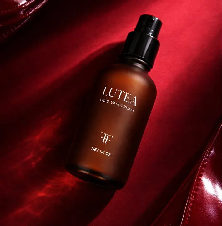 A brown bottle of Lutea Wild Yam Cream with a black pump top, on a rich red background.