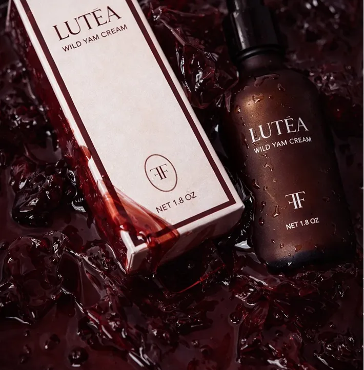 A bottle and box of Lutea Wild Yam Cream sit in a dark red, viscous liquid.