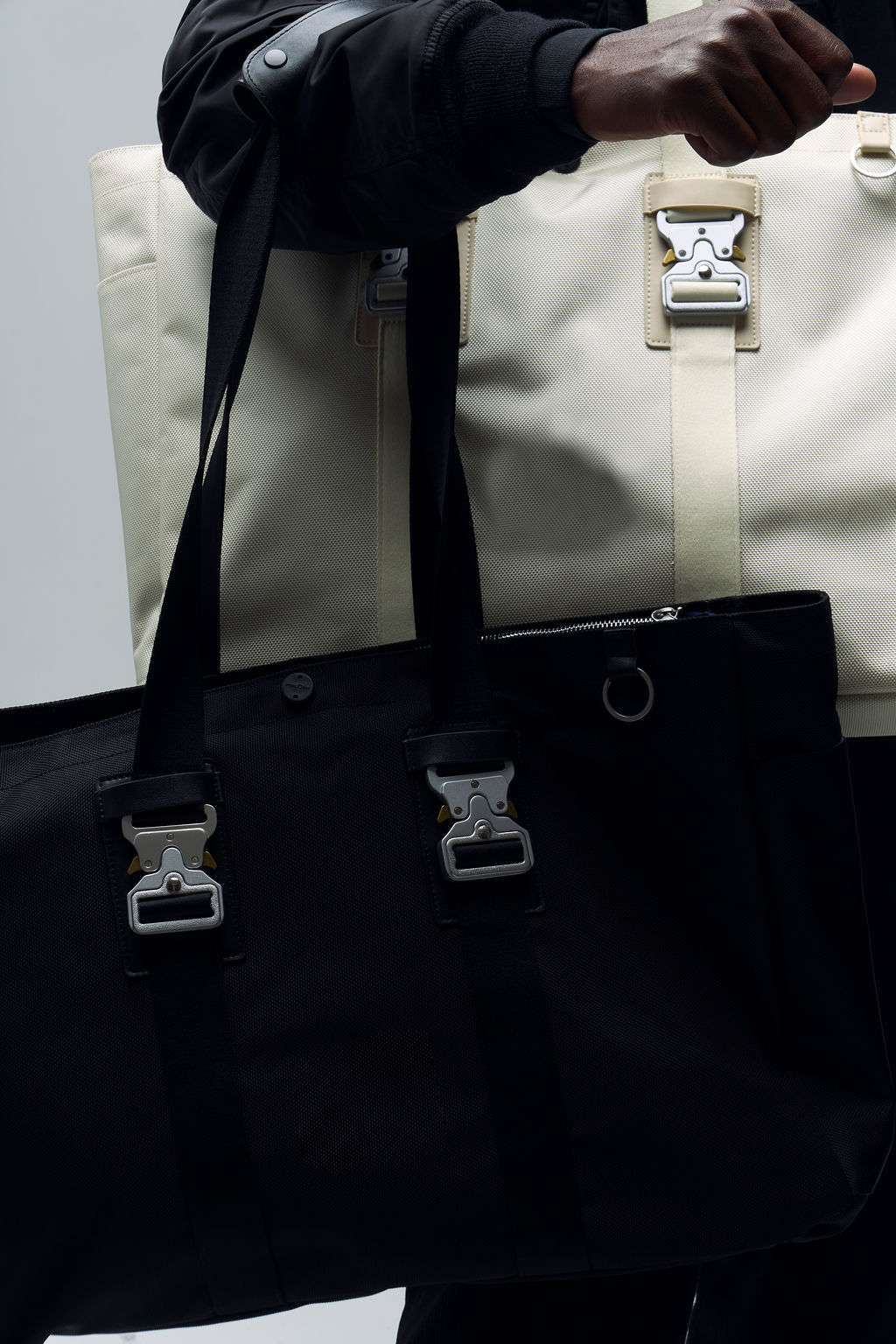 Person holding black and white bags with metal buckles.
