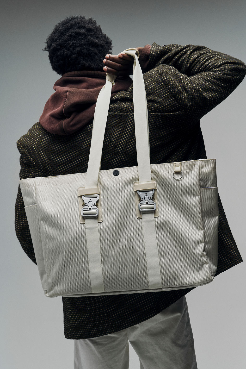 Person holding a large beige tote bag over their shoulder.